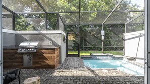 An outdoor patio with a barbecue grill, a wooden cabinet, and a swimming pool. - 4BR Le Reve Pool & Themed Rooms Near Disney (Kissimmee)