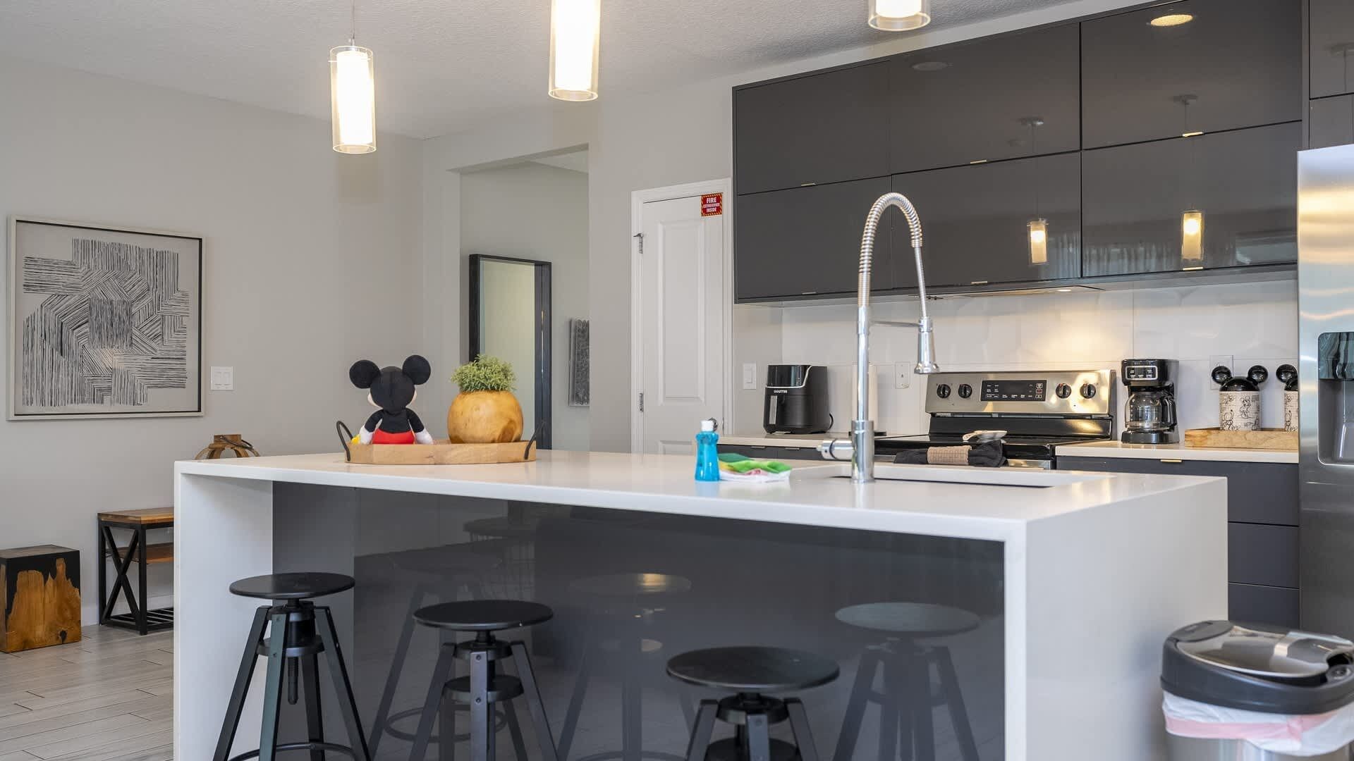 A modern kitchen with a central island, bar stools, a coffee machine, and a fire exit door.
