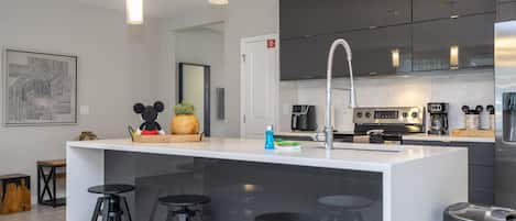 Cocina moderna con una isla central, taburetes de bar, una cafetera y una puerta de salida de incendios.