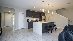 A modern kitchen with a central island, bar stools, and a staircase leading to an upper level. - 4BR Le Reve Pool & Themed Rooms Near Disney (Kissimmee)