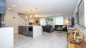 A modern living room with a sofa, a coffee table, and a kitchen area with a sink and appliances. - 4BR Le Reve Pool & Themed Rooms Near Disney (Kissimmee)