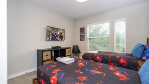 A bedroom with two beds, a TV, a bookshelf, and a window with blinds. - 4BR Le Reve Pool & Themed Rooms Near Disney (Kissimmee)