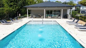 Una piscina rectangular con agua azul cristalina, rodeada de sillas de descanso y una zona de estar cubierta.