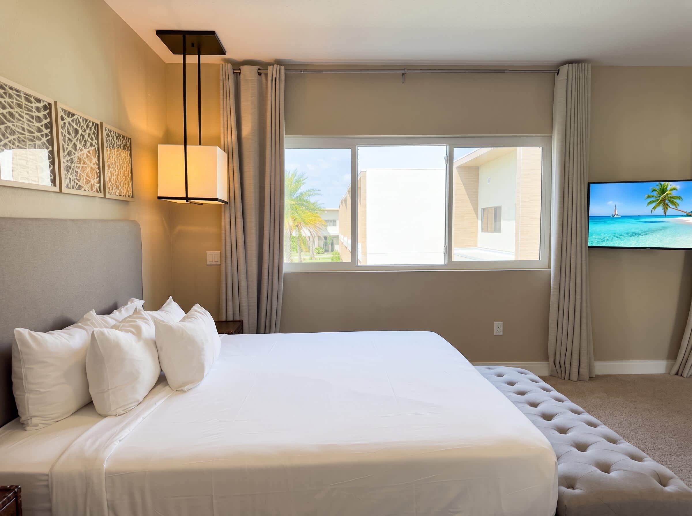 Habitación de hotel con una cama grande, televisión y ventana con vista a edificios y palmeras.