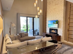 Ein modernes Wohnzimmer mit einer Couch, einem Glastisch, einem Kamin und einem an einer Ziegelwand befestigten Fernseher.