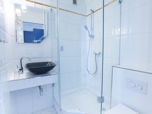 Ein modernes Badezimmer mit einer gläsernen Duschkabine, einem schwarzen Waschtischbecken und einem weißen Waschtisch.