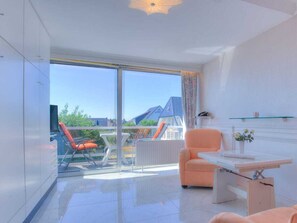 Ein modernes Zimmer mit Glastür zu einem Balkon, einem kleinen Tisch, einem Stuhl und einer Vase mit Blumen.