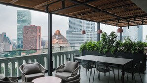 Ein Sitzbereich im Freien mit Korbmöbeln und einem Tisch, mit Blick auf eine Skyline moderner Gebäude.