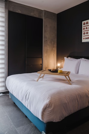 Un dormitorio moderno con una cama grande, una bandeja de madera con alimentos para el desayuno y una obra de arte colgada en la pared.