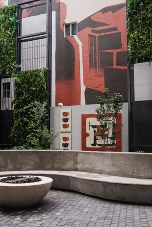 A building facade with a large mural, a barred window, and a concrete planter with a tree. - Loft one block from the Monumento a la Revolución, between Centro Histórico and Reforma. Private balcony, rooftop with incredible views, gym, garden, and a coworking area among the shared amenities. (Tabacalera)