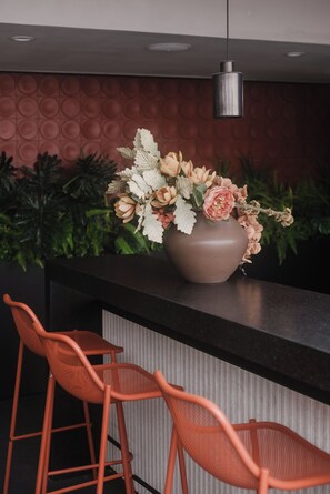 A bar area with a large vase of flowers, two orange chairs, and a modern pendant light. - Loft one block from the Monumento a la Revolución, between Centro Histórico and Reforma. Private balcony, rooftop with incredible views, gym, garden, and a coworking area among the shared amenities. (Tabacalera)