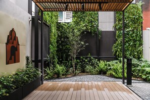 A wooden deck leading to a covered patio area with a view of a garden and a building in the background. - Loft one block from the Monumento a la Revolución, between Centro Histórico and Reforma. Private balcony, rooftop with incredible views, gym, garden, and a coworking area among the shared amenities. (Tabacalera)