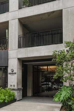 A modern building with a concrete facade, a visible entrance with glass doors, and a sign indicating 'SENNSE TABACALERA'. - Loft one block from the Monumento a la Revolución, between Centro Histórico and Reforma. Private balcony, rooftop with incredible views, gym, garden, and a coworking area among the shared amenities. (Tabacalera)