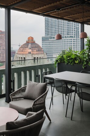 Un área de estar exterior moderna con sillas de mimbre y una mesa, con vistas a un paisaje urbano donde destaca un edificio con forma de cúpula.