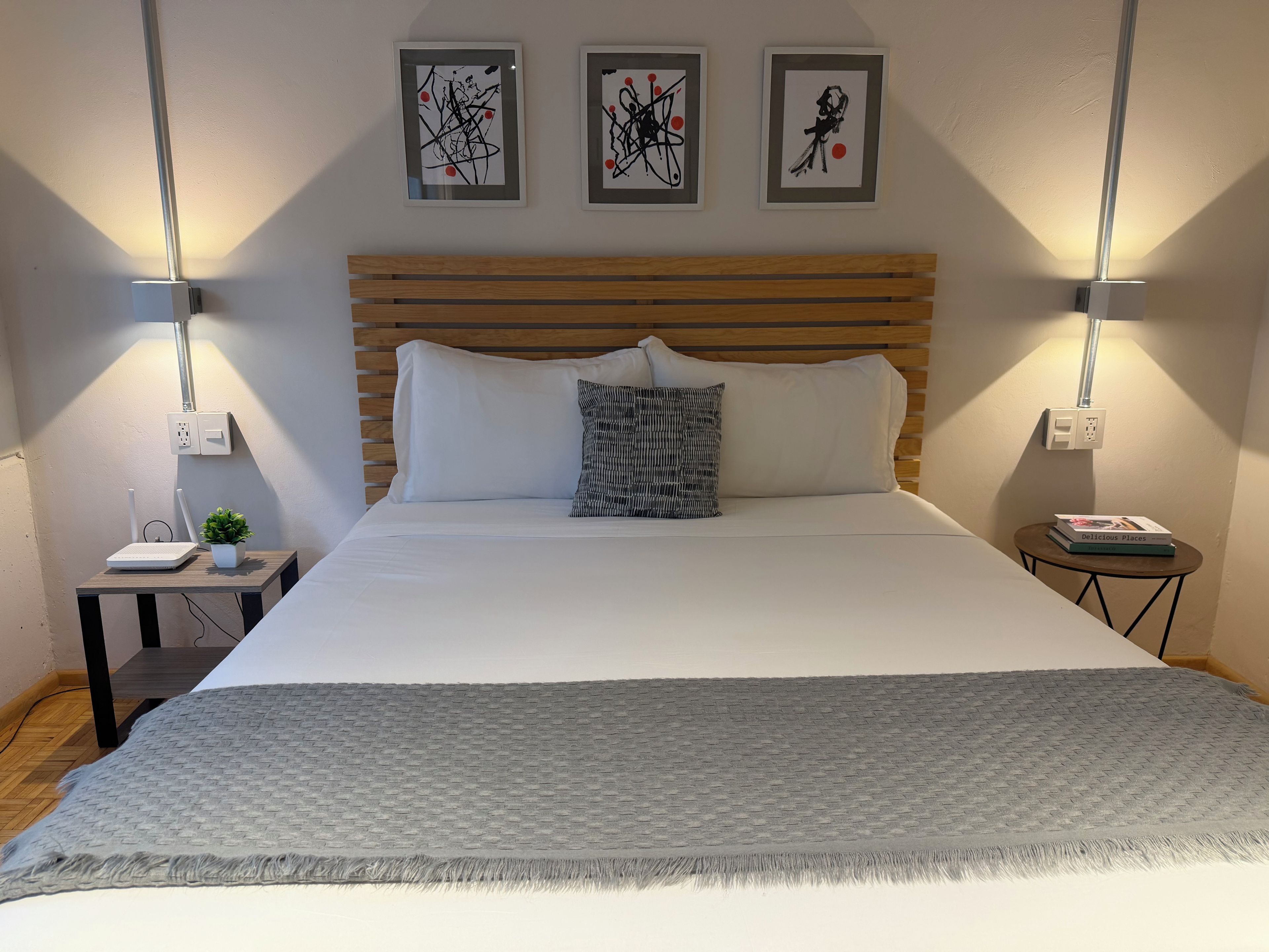 A neatly made bed with a grey textured blanket, a wooden headboard, and two wall-mounted lamps.