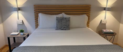 A neatly made bed with a grey textured blanket, a wooden headboard, and two wall-mounted lamps.