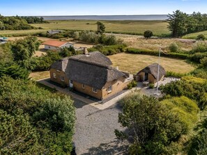 A house with a thatched roof, surrounded by a gravel driveway and lush greenery. - "Helma" - 580m to the fjord by Interhome (Ulfborg)