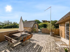 An outdoor patio with a wooden table and benches, a thatched-roof building, and a clear sky. - "Helma" - 580m to the fjord by Interhome (Ulfborg)