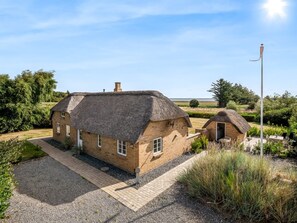Une maison traditionnelle à toit de chaume, avec une allée en gravier et une petite construction adjacente.
