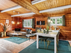 Un intérieur de chalet chaleureux avec un coin repas, des sièges et une grande fenêtre.