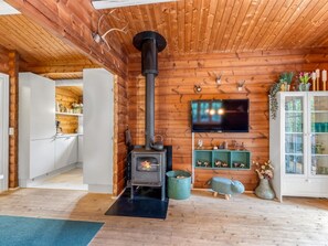 L’intérieur d’une cabane en rondins, avec un poêle à bois, un coin cuisine et un téléviseur fixé au mur.
