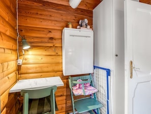 Ein Holzblockhaus-Innenraum mit einer weißen Tür, einem kleinen Tisch, einem Stuhl und einem Spielplatz für Kinder.