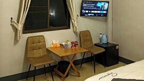 A hotel room with a bed, a TV, a small table with chairs, an air conditioner, and a window with curtains.