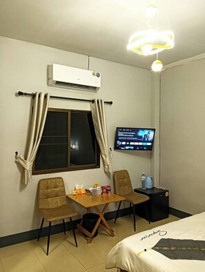 A hotel room with a bed, a TV, a small table with chairs, an air conditioner, and a window with curtains.