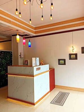 A reception desk with a marble top, a red accent wall, and a wooden ceiling.