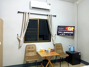 A small room with a window, a flat-screen TV, a table with chairs, and a black suitcase.