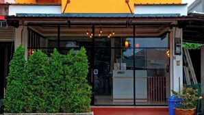 A building with a bright yellow facade, a covered entrance, and a small garden area with a bush and a potted plant.