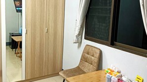 A room with a wooden wardrobe, a window with curtains, a table with various items, and a mirror reflecting a TV and a table.
