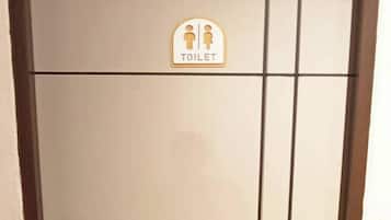 Een deur met een toiletbord, een deurklink en een ventilatie rooster.