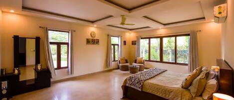 A spacious bedroom with a large bed, a desk, and a chair. There are multiple windows providing natural light.