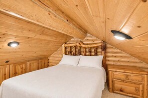 A wooden interior with a bed, a nightstand, and a ceiling light.