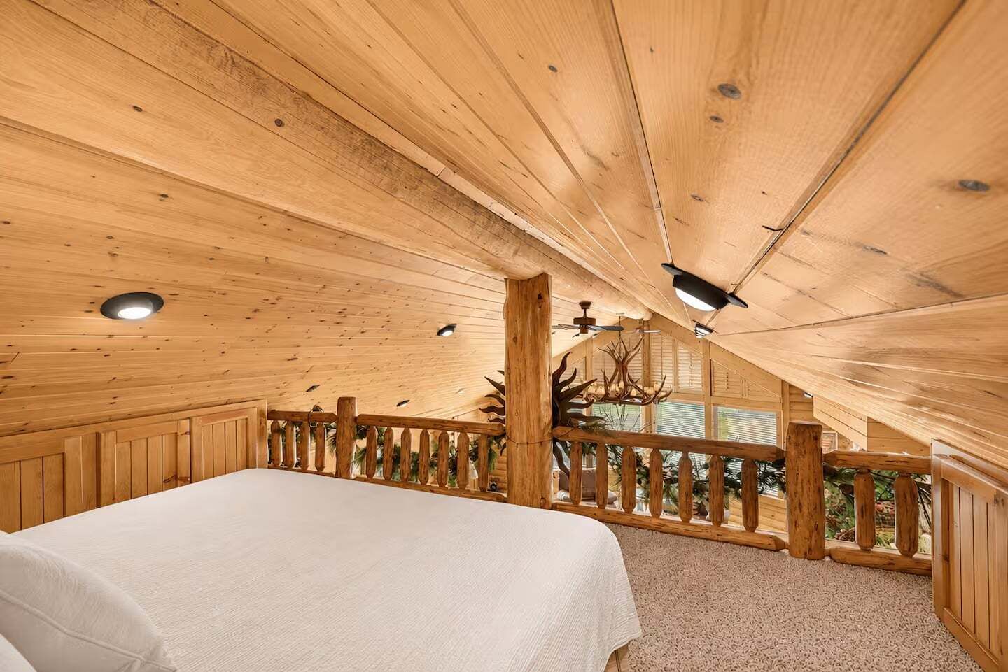 A wooden cabin bedroom with a bed, a balcony with a railing, and a ceiling fan.