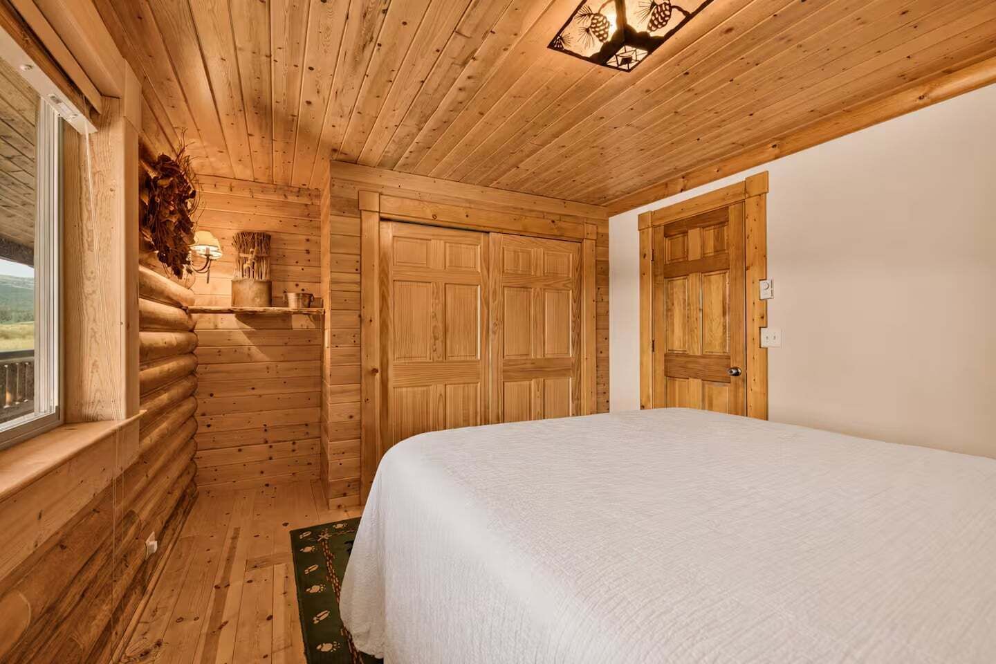 A log cabin room with a bed, wooden walls, a window, and a door.