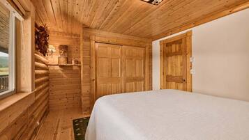 A log cabin room with a bed, wooden walls, a window, and a door.