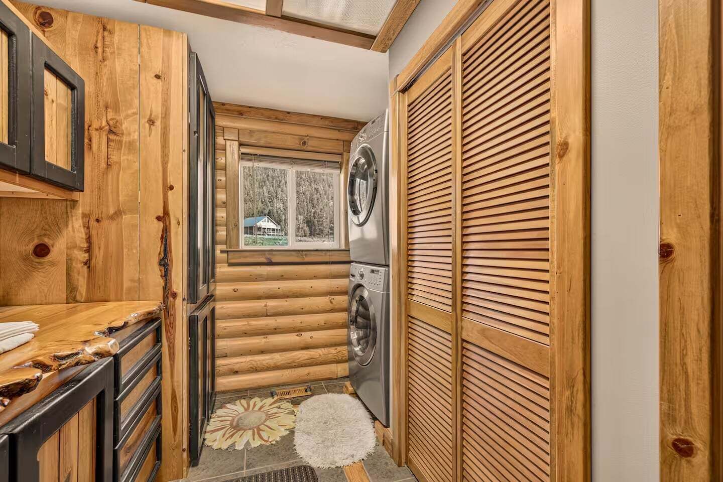 A compact kitchen with wooden walls, a washing machine, and a window with a view of a house.
