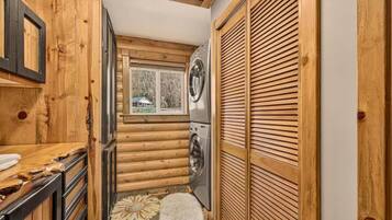A compact kitchen with wooden walls, a washing machine, and a window with a view of a house.