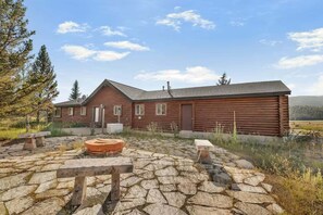 A rustic log cabin with a stone patio and a fire pit.