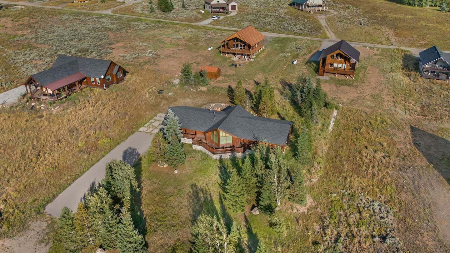 A cluster of log cabins with a central building featuring a large deck and a stone pathway leading to it.