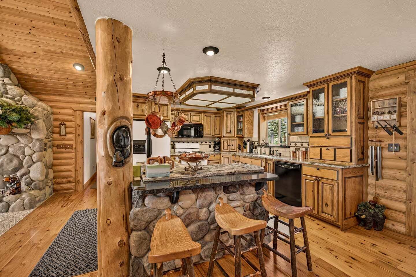 A rustic kitchen with wooden cabinets, a stone island, and bar stools.