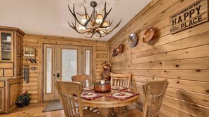 Interior de una cabaña de madera con una mesa de comedor, sillas, una araña y un cartel en la pared.