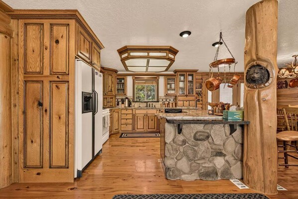 A kitchen with wooden cabinets, a stone island, and copper cookware.