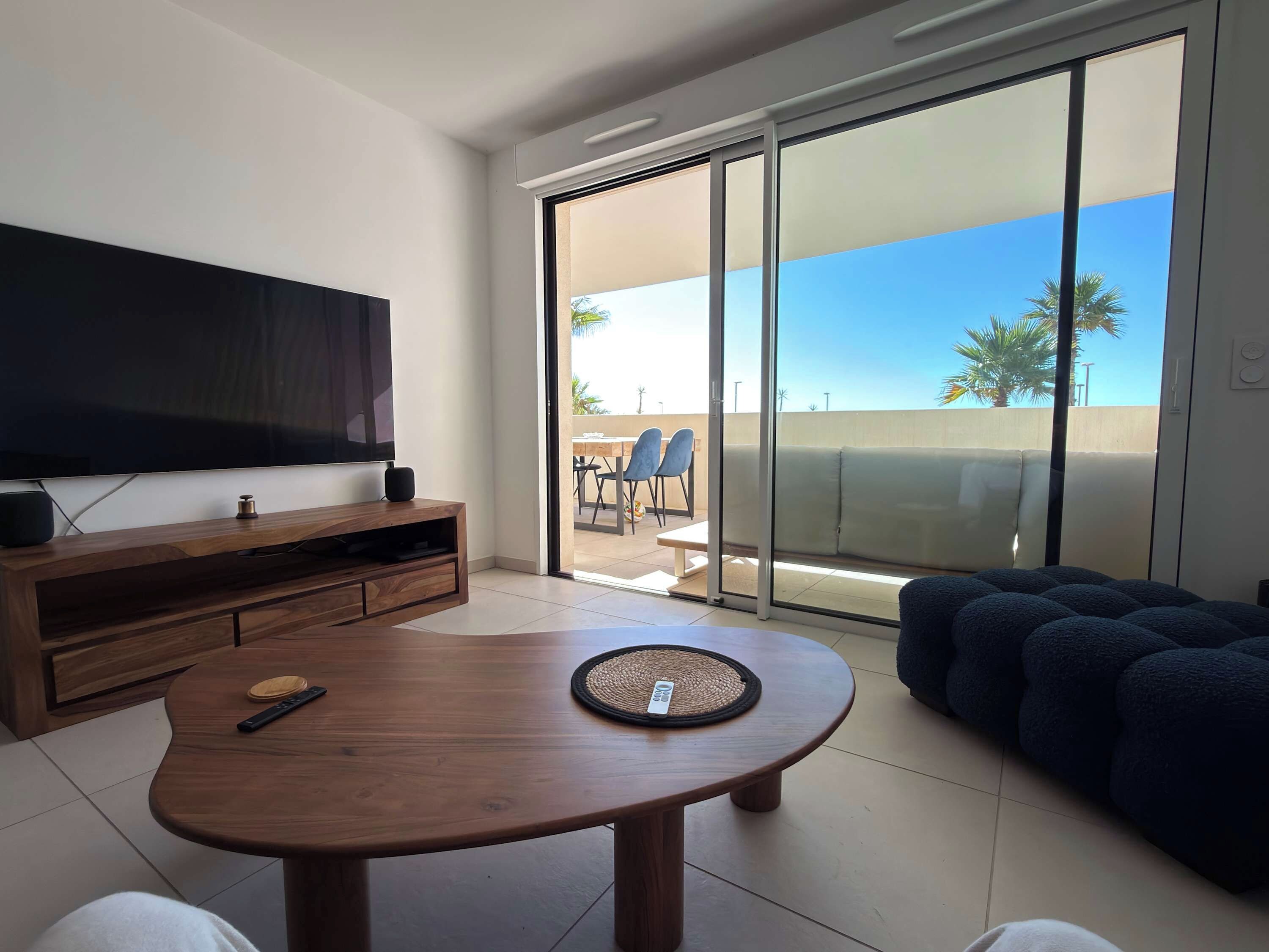 A modern living room with a flat-screen TV, wooden entertainment unit, round coffee table, and a dark blue sofa.