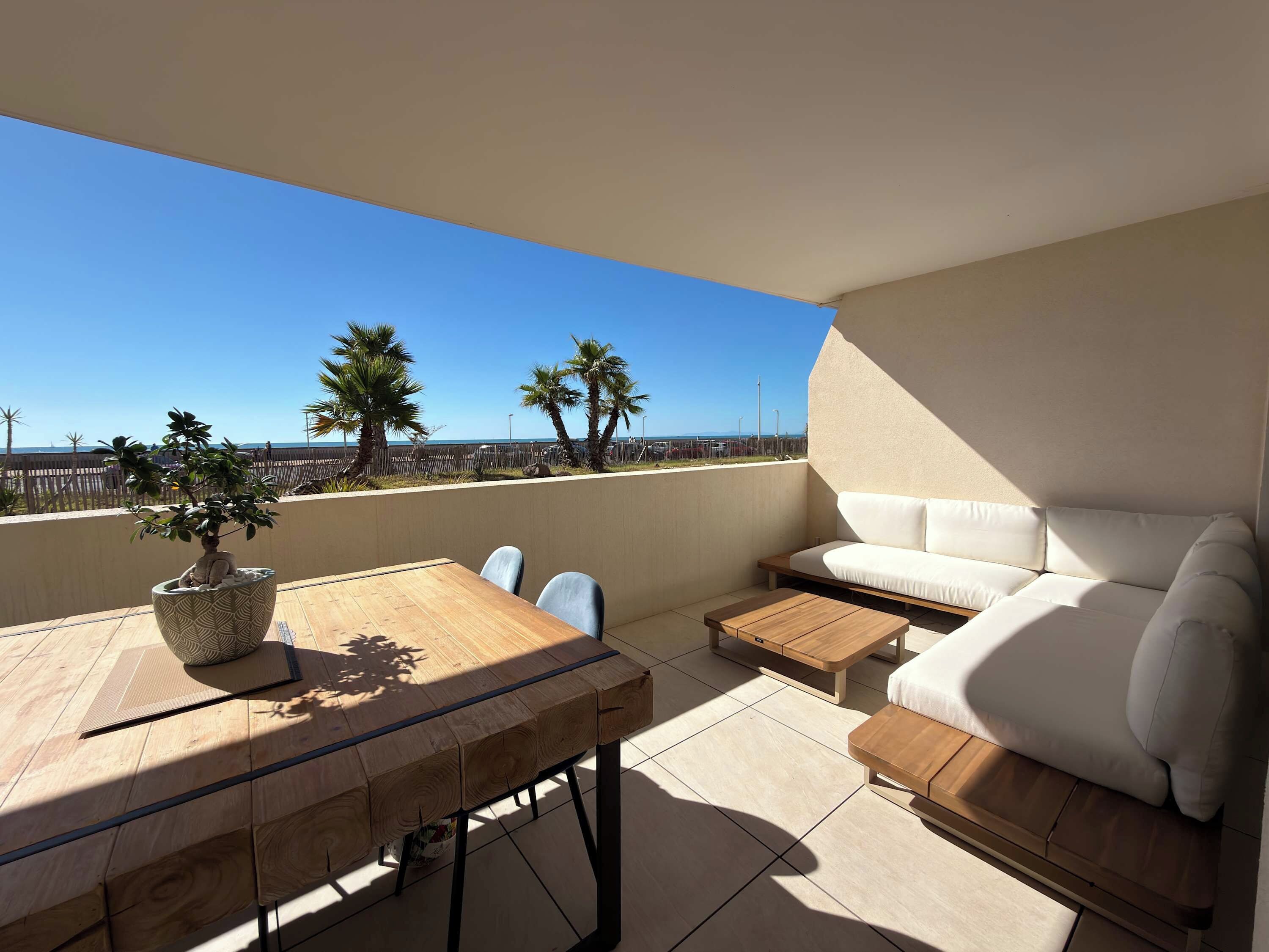 A balcony with a wooden table, a white sofa, and a potted plant.