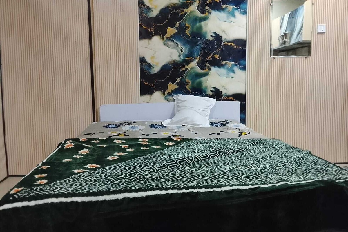 Una cama con colcha estampada y manta decorativa, una pared con diseño que imita el mármol, y un espejo en la pared.