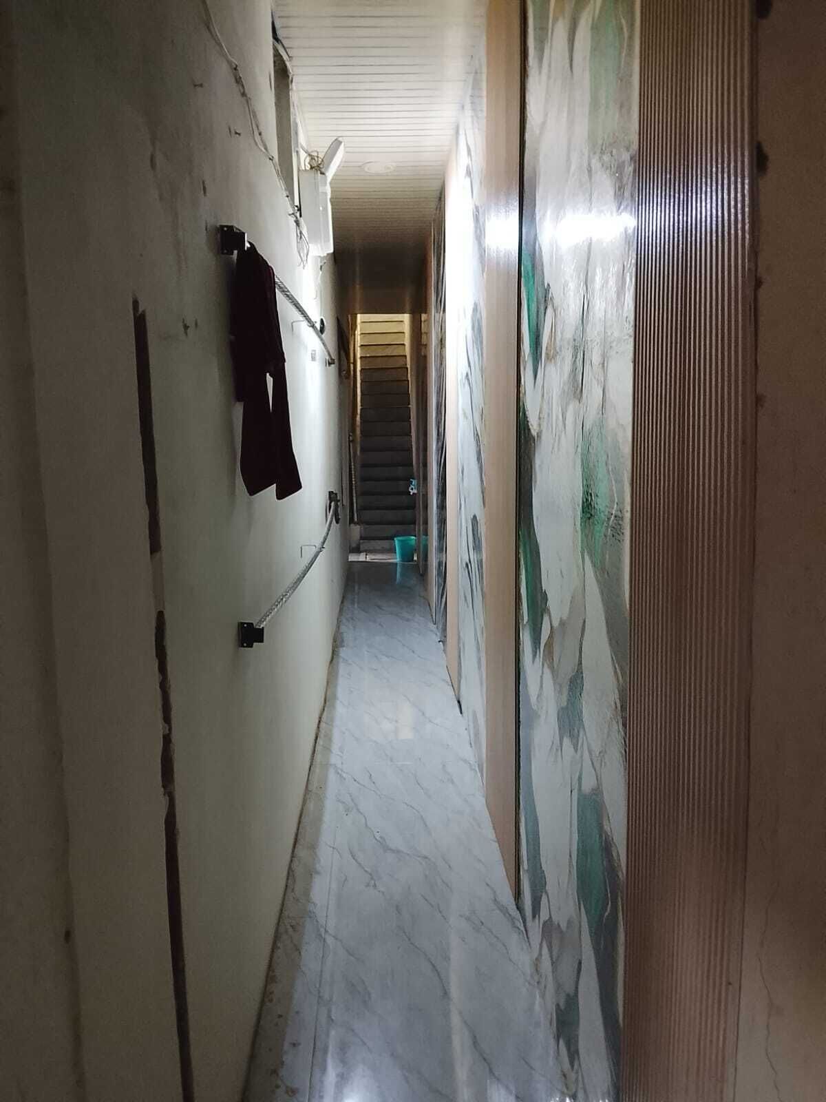 Un pasillo estrecho con una escalera al final, un perchero en la pared y un cubo de basura verde.