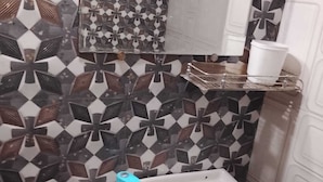 A bathroom with a white sink, a mirror, and a patterned tile wall. - Hotel Welcome (Indore)